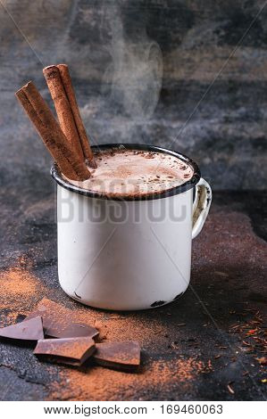 Vintage mug of hot chocolate with cinnamon sticks over dark background