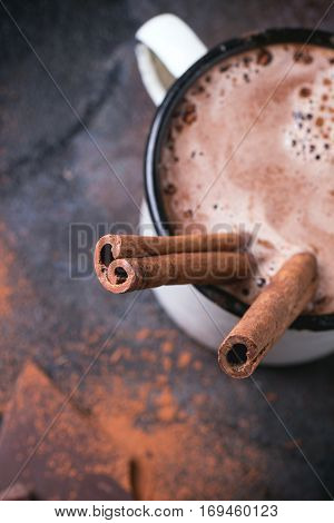 Vintage mug of hot chocolate with cinnamon sticks over dark background. Focus on cinnamon. Top view.