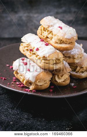 Ceramic plate of mini eclairs with white chocolate, served with dry raspberry on dark background