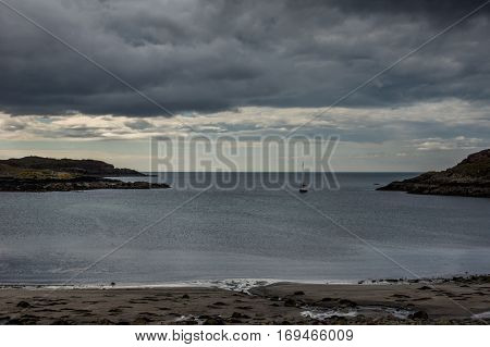Northwest Coast Scotland - June 6 2012: Scourie Bay as part of the Atlantic Ocean in the evening during twilight. A sail boat returns to the harbor. Rocky shores and a cloudscape of rain. Far out light blue sky.
