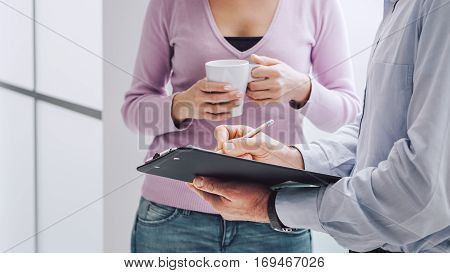 Business people having a briefing during a coffee break a woman is holding a cup of coffee her collegue is holding a clipboard and pointing with a pencil
