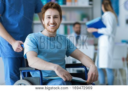 Smiling disabled young man on wheelchair at the hospital a doctor is assisting him