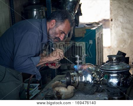 KASHAN IRAN - AUGUST 13 2016: Crafstman reparing a samovar in Kashan bazaar Iran Samovars (sometimes also spelled Samavar or Samaavar) are used to boil water for tea and are a staple in most Persian homes.
