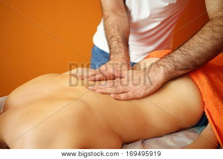 Masseur in white massages back of young woman in room, noface