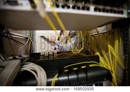 Technician using digital tablet while analyzing server in server room