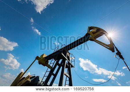 Oil field with pump jack, profiled on blue sky with white clouds, on a sunny day in spring