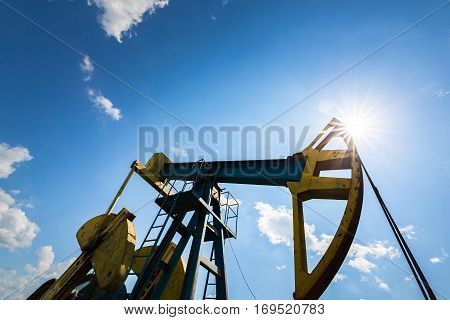 Oil field with pump jack, profiled on blue sky with white clouds, on a sunny day in spring