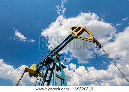 Oil field with pump jack, profiled on blue sky with white clouds, on a sunny day in spring