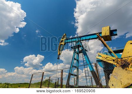Oil field with pump jack, profiled on blue sky with white clouds, on a sunny day in spring