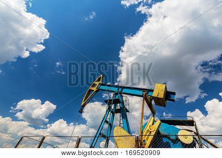 Oil field with pump jack, profiled on blue sky with white clouds, on a sunny day in spring