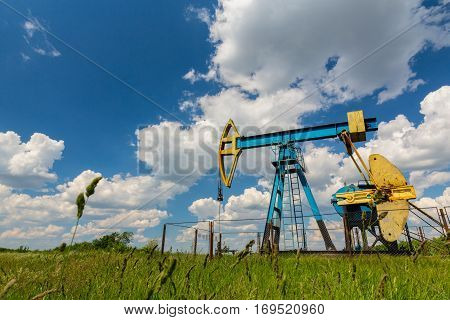 Oil field with pump jack, profiled on blue sky with white clouds, on a sunny day in spring