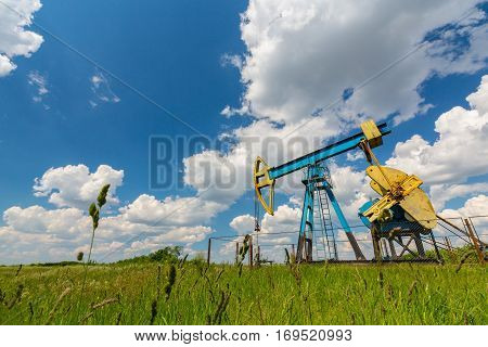 Oil field with pump jack, profiled on blue sky with white clouds, on a sunny day in spring