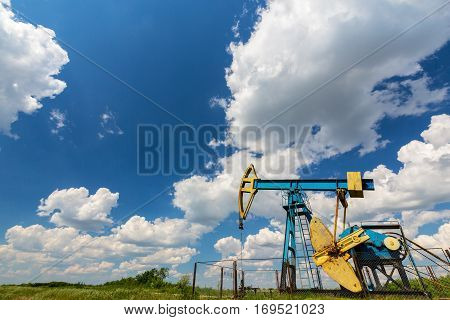 Oil field with pump jack, profiled on blue sky with white clouds, on a sunny day in spring