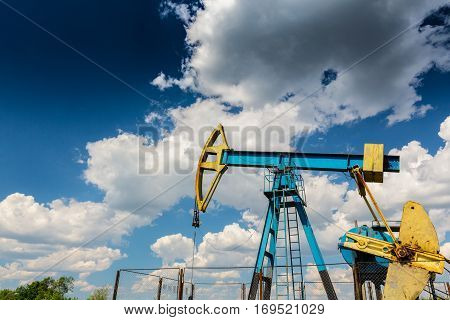 Oil field with pump jack, profiled on blue sky with white clouds, on a sunny day in spring