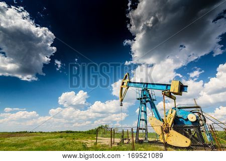 Oil field with pump jack, profiled on blue sky with white clouds, on a sunny day in spring