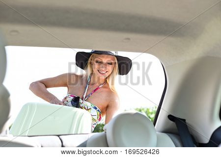 Happy woman loading suitcase in car trunk