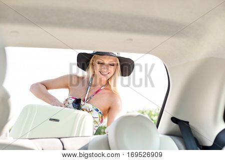 Happy woman loading suitcase in car trunk