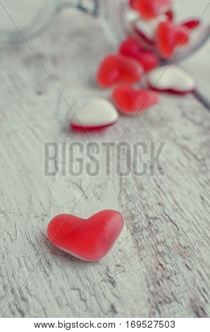 Red heart shape candy in a glass jar on a white rustic wooden table with space for text. Romantic love concept. Valentine's Day greetings card. Valentines theme. Selective focus. Copy space.