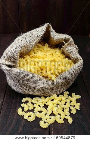 Raw macaroni (Pasta Galetti) big pile in the sack on a wooden table.
