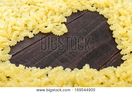 Raw macaroni - pasta Galetti. In the middle of the empty space in the shape of a heart on a dark wooden background.