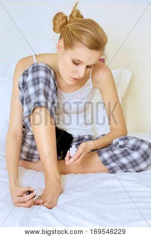 young woman sitting and applying nail polish on toe nails