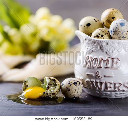 Bunch of quail eggs in the vase. Broken egg nearby. The gray background.