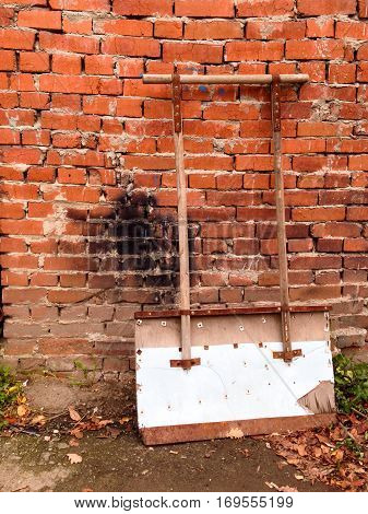 Shovel for snow cleaning is waiting for work near brick wall