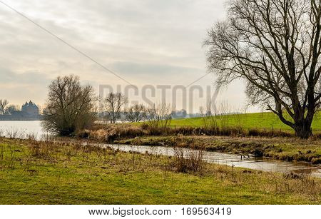 Picturesque Dutch river landscape in autumnal colors. Across the wide river is the famous castle Loevestein in the background. It si a cloudy day in the winter season.