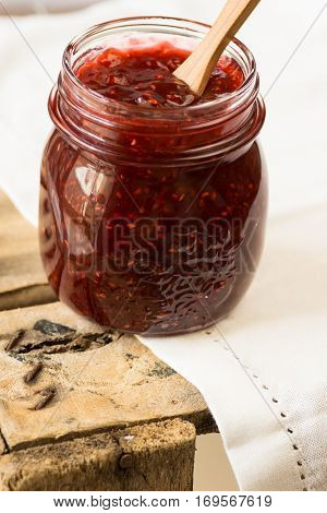 Jar with homemade raspberry jam,spoon dipped into the confiture, on vontage wood box,white linen napkin,cozy morning, breakfast
