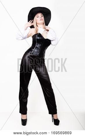 sexy woman with hourglass figure dressed in black leather corset and pants with wide-brimmed hat.