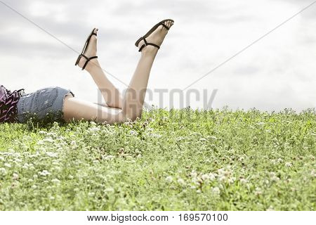 Low section of woman lying on grass against sky
