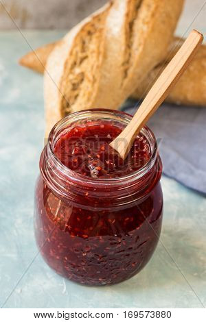 Mason jar with homemade raspberry marmalade with wooden spoon, wholemeal rolls on a linen napkin, breakfast, cozy atmosphere