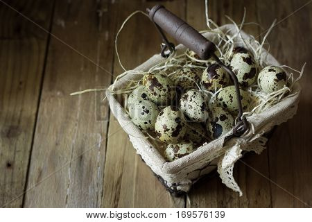 Quail eggs in a lined wire basket, on straw, on barn wood background, Easter, rustic vintage style, kinfolk, simplicity, countryside interior, selective focus, top view