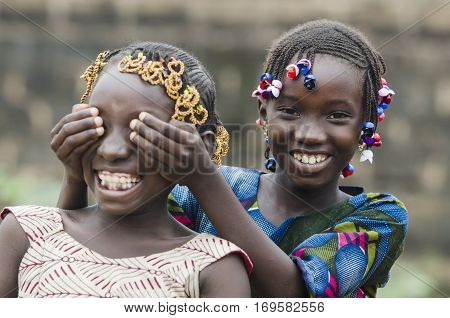 Two young african girls with traditional accessories in hair having fun in front of camera playing peekaboo