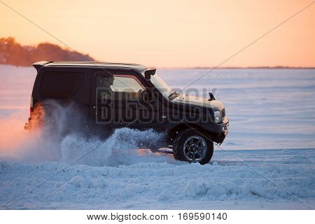 KHABAROVSK RUSSIA - JANUARY 28 2017: Suzuki Jimny moving on ice of a frosn river at sunset