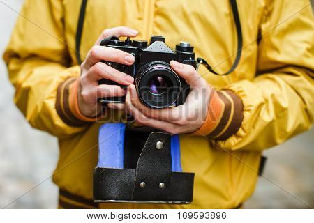 A young guy hipster, holding oldschool film camera, day outdoors, close up, center frame, makes photo