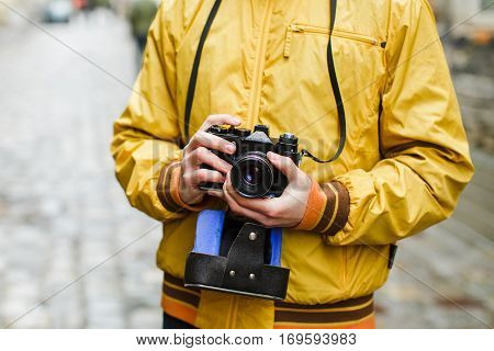 A young guy hipster, holding oldschool film camera, day outdoors, close up, center frame, makes photo