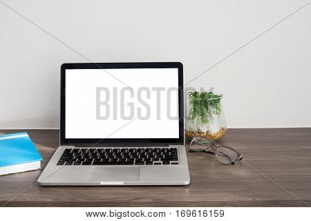Office desk with blank screen on laptop cover blue notebook paper modern eyeglasses garden tree on pot and cement wall background. concept of business lifestyle.