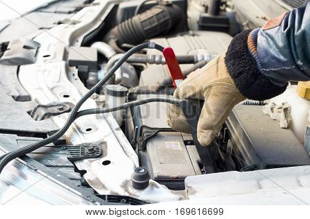 Driver hand wearing warm gloves holding the jump leads next to the flat car battery