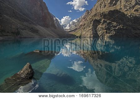 Blue lake surrounded with rocks. Blue sky and clouds reflects in water. Big Alo is the most beauty lake of Fann Mountains