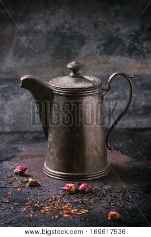 Vintage teapot with dry tea and rose buds over black metal background