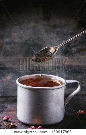Vintage aluminum mug with flowing hot tea with tea strainer over dark background