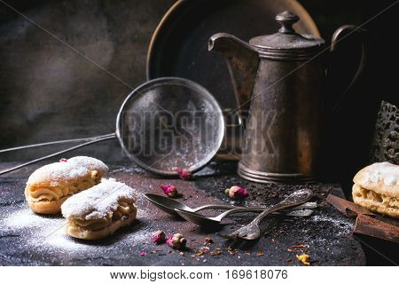 Tea drinking with eclairs and chopped chocolate, served with vintage teapot and cutlery over dark background. See series