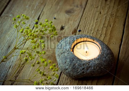 Stone candle holder with tea light on aged wood background, delicate spring yellow flowers, Easter, tranquility concept,meditation