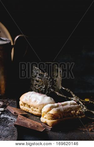 Tea drinking with eclairs and chopped chocolate, served with vintage teapot and cutlery over dark background. See series