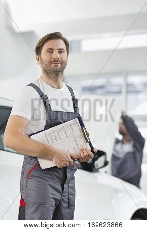 Portrait of confident male automobile mechanic with clipboard in car repair store