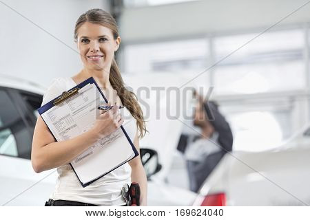 Portrait of smiling female repair worker with clipboard in car workshop