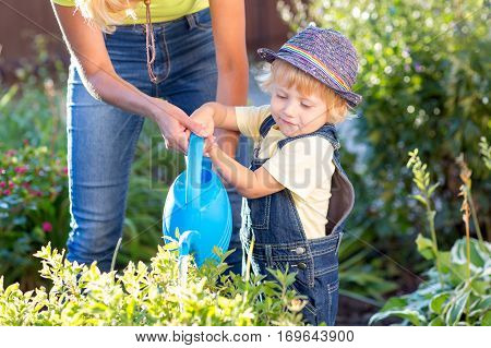 Kid with mom in garden. Child watering flowers. Mother helps little son.