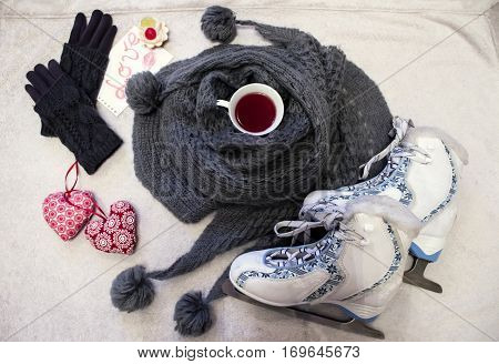 White-blue figure skates warm gray skarf with pompons cup of tea knitted gloves and cute textile hearts
