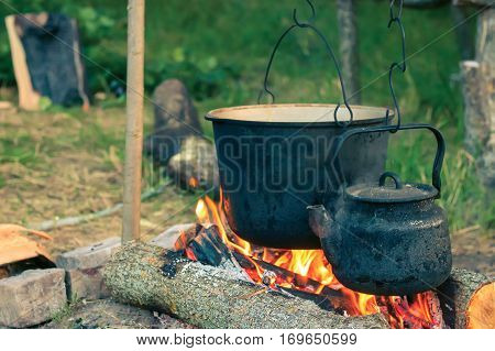 Two smoked tourist kettles over camp fire. Process of cooking on the nature. vintage filtered